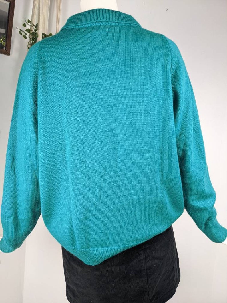 May include: A teal blue knitted sweater with long sleeves and a crew neck.