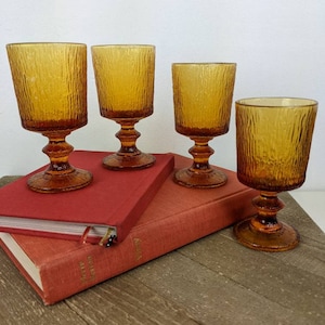 May include: Four amber-coloured vintage wine glasses with textured sides and a pedestal base. The glasses are arranged on top of two red books. The glassware is ideal for serving wine. Each glass is approximately 15 cm tall.