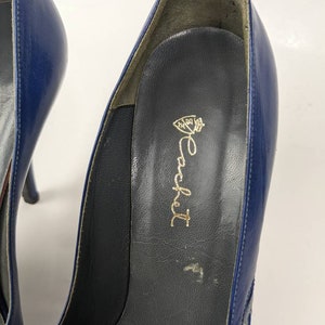 May include: Close-up of the inside of a blue leather high-heeled shoe with a gold inscription that reads "Rocket" with a crown above the word.