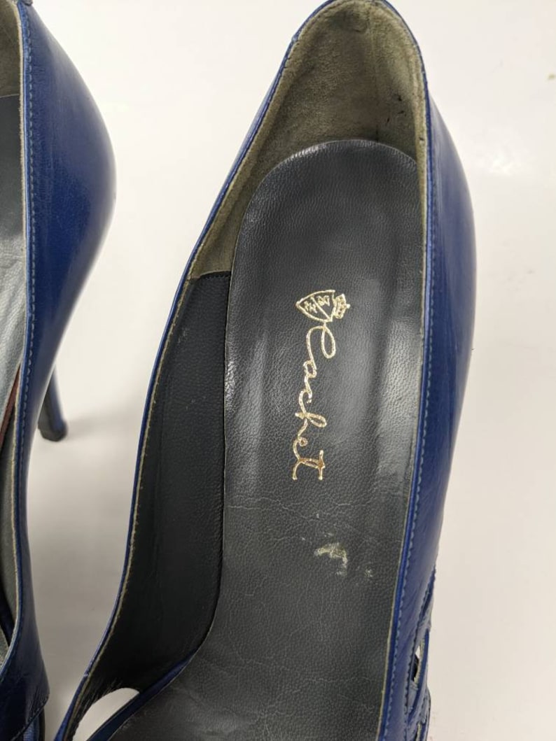 May include: Close-up of the inside of a blue leather high-heeled shoe with a gold inscription that reads "Rocket" with a crown above the word.