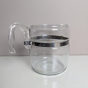 May include: A clear glass percolator coffee pot with a silver metal band around the middle and a glass handle.