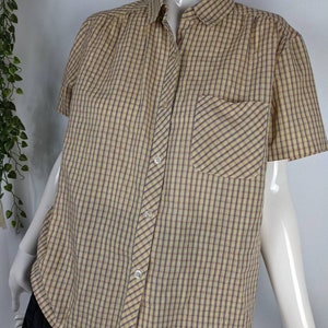 May include: A yellow and purple checked short-sleeved button-down shirt with a single chest pocket.