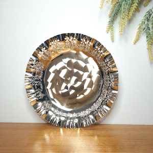 May include: A silver serving dish with a scalloped edge and a floral design. The dish is made of metal and has a shiny finish.