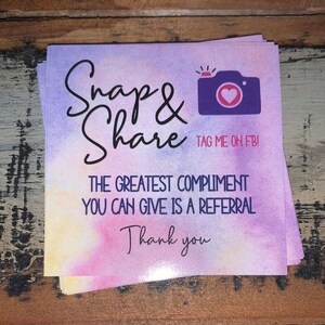 May include: A purple and pink watercolor background with the text "Snap & Share" and a purple camera with a pink heart. The text "TAG ME ON FB!" is below the camera. The text "THE GREATEST COMPLIMENT YOU CAN GIVE IS A REFERRAL" is below the camera. The text "Thank you" is at the bottom of the image.