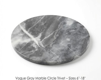 May include: A circular trivet made of gray marble with white veining. The surface features a natural stone pattern with varying shades of gray. The text below the object reads: Vogue Gray Marble Circle Trivet – Sizes 6"-18".