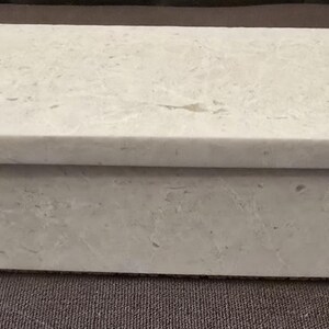 Puede incluir: Una caja rectangular blanca con una superficie texturizada. La caja est&aacute; hecha de un material que se asemeja al m&aacute;rmol.