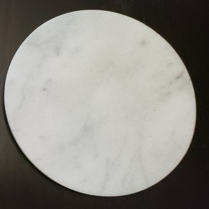 May include: A white round marble coaster with a subtle grey veining pattern.