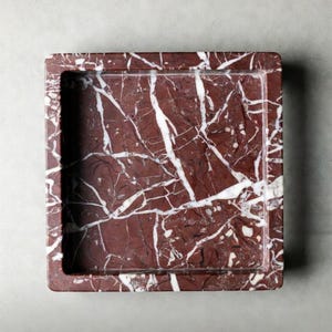 May include: A square Rosso Levanto marble tray featuring a deep burgundy red base with prominent white veining throughout. The tray has a recessed center and thick edges. The text on the image reads: Rosso Levanto Marble Tray 6" x 6" x 1".