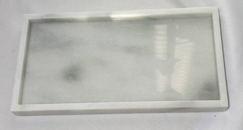 May include: A white rectangular tray with a raised rim. The tray has a subtle marbled pattern with gray streaks throughout.