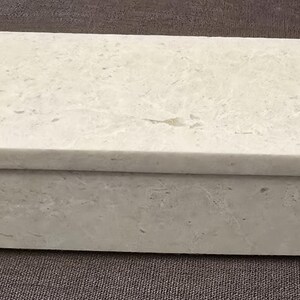 Puede incluir: Una caja rectangular blanca con tapa. La caja est&aacute; hecha de un material texturizado que se asemeja a la piedra.