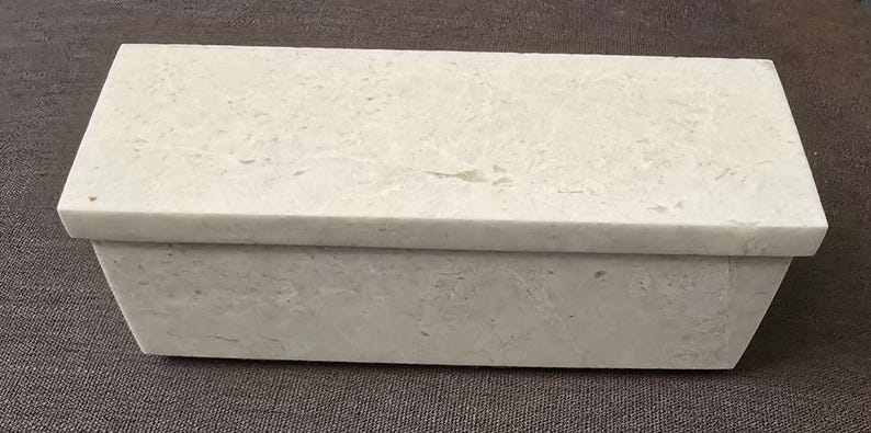 Puede incluir: Una caja rectangular blanca con tapa. La caja est&aacute; hecha de un material texturizado que se asemeja a la piedra.
