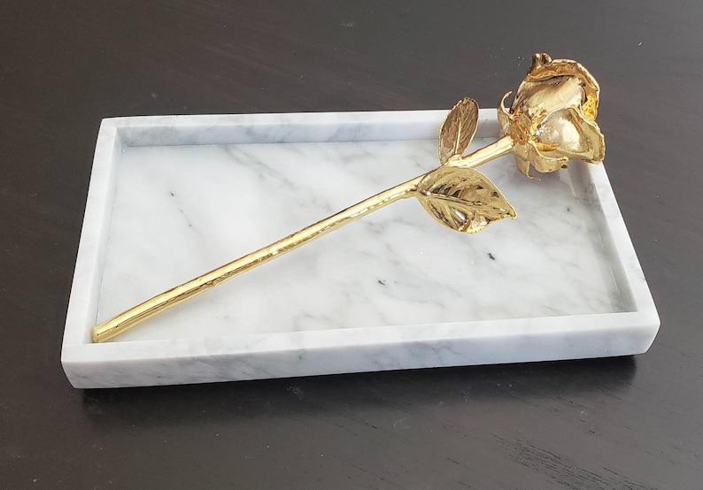 May include: A gold-plated rose on a white marble tray. The rose is a single stem with a single bloom and leaves.