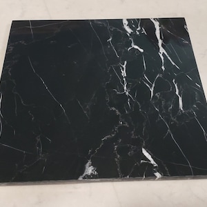 May include: A black marble cutting board with white veining. The board is square and has a smooth surface.