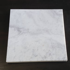 May include: A white square tile with a subtle grey veining pattern.