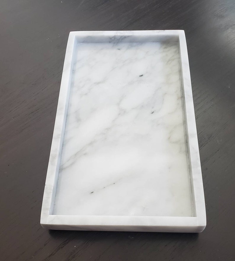 May include: A white marble tray with a raised border. The tray is rectangular and has a smooth surface.