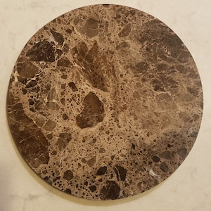 May include: A round, brown marble coaster with a speckled pattern. The coaster is made of natural stone and has a smooth, polished surface.