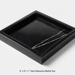Può includere: Un vassoio quadrato in marmo Nero Marquina, 15 cm per 15 cm, con una profondità di 2,5 cm. Il vassoio è nero con venature bianche e ha un bordo rialzato. Adatto per servire o esporre.