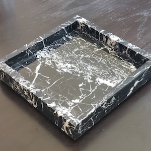 May include: A square black marble tray with white veining. The tray has a raised edge.