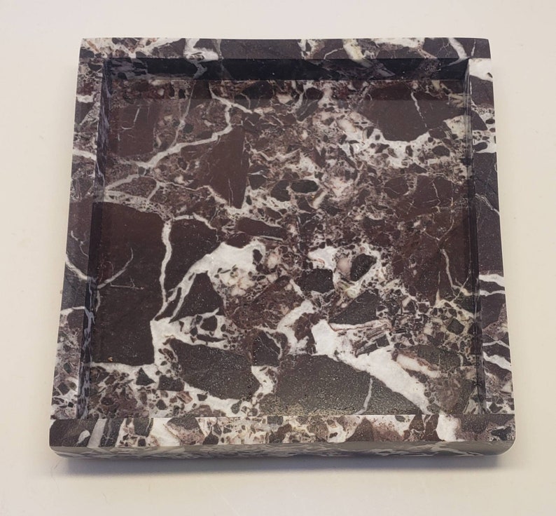 May include: A square tray crafted from dark brown and black stone with prominent white veining throughout. The tray features a flat base and raised edges, showcasing a natural, polished, and multi-tonal marbled pattern across its entire surface.