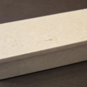Puede incluir: Una peque&ntilde;a caja rectangular hecha de piedra blanca con una superficie texturizada. La caja tiene una tapa con bisagras y est&aacute; cerrada.