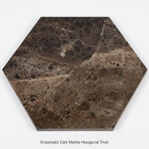 Könnte beinhalten: Sechseckiger Emperador Dark Marble Untersetzer. Der Untersetzer hat ein dunkelbraunes Marmormuster mit hellbraunen und beigen Adern. Der Untersetzer hat eine sechseckige Form und ist vor einem weißen Hintergrund platziert.