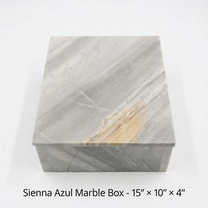 May include: A rectangular Sienna Azul marble box with a smooth, polished surface featuring grey and white veining and a prominent golden-brown streak. The box measures 15 inches by 10 inches by 4 inches as indicated by the text at the bottom.