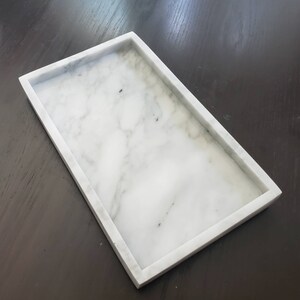 May include: A white marble rectangular tray with a smooth surface and slightly raised edges.