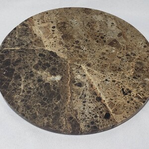 May include: Round brown marble serving tray with a mottled pattern. The tray is perfect for serving appetizers, cheese, or other small items.