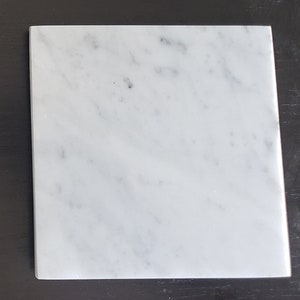 Könnte beinhalten: Ein weißes Marmor-Schneidebrett mit einer glatten Oberfläche und subtilen grauen Adern.