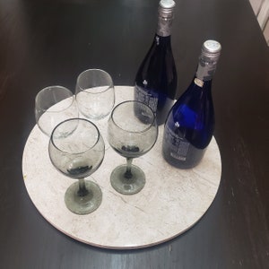 Può includere: Un vassoio rotondo in marmo beige con quattro bicchieri di vetro trasparente e due bottiglie di vetro blu. Le bottiglie hanno tappi argentati ed etichette.