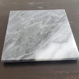 Könnte beinhalten: Ein quadratisches Serviertablett aus grauem und weißem Marmor mit einem geäderten Muster.