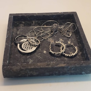 May include: A black marble jewelry tray with silver jewelry, including a chain necklace with a pendant, a ring, and two hoop earrings.