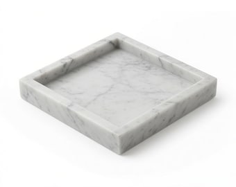 May include: A square Bianco Carrara marble tray with a white base and grey veining. The tray features raised edges and measures 6 inches by 6 inches by 1 inch as indicated by the text printed below the object on the white background.