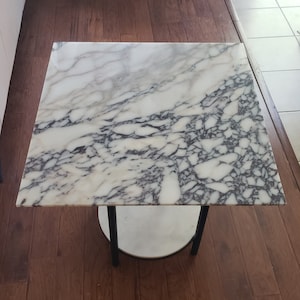 May include: A white marble top side table with a black metal frame. The table has a round lower shelf.