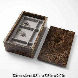 May include: A rectangular jewelry box with a brown marble pattern finish and a removable lid. The interior features a light gray velvet lining with multiple compartments for organization. The box measures 8.5 inches by 5.5 inches by 2.0 inches.