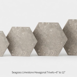 May include: Four hexagonal trivets made of seagrass limestone, ranging in size from 6 to 12 inches. The trivets are a light gray color and have a textured surface. The trivets are arranged in a row, with the smallest on the left and the largest on the right.