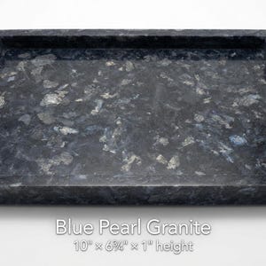 May include: A rectangular Blue Pearl granite tray with a polished surface featuring dark blue, black, and shimmering silver mineral flecks. The tray measures 10 inches by 6.25 inches by 1 inch in height, as indicated by the text printed below it.