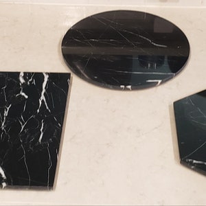 May include: Three black marble serving trays with white veining. The trays are round, square, and hexagonal.