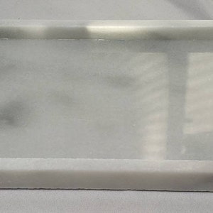 May include: A white marble rectangular tray with a raised rim. The tray is smooth and has a subtle gray veining.