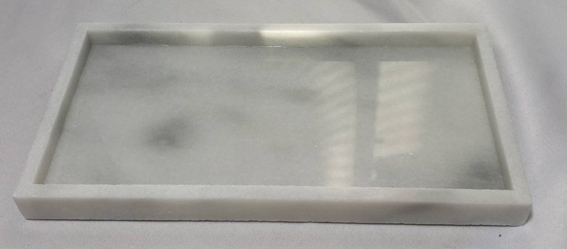 May include: A white marble rectangular tray with a raised rim. The tray is smooth and has a subtle gray veining.