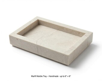 May include: A rectangular Marfil marble tray with a light beige color and natural veining. The tray features a recessed center and raised edges. The text printed below the object reads: Marfil Marble Tray - Handmade - up to 6" x 6".