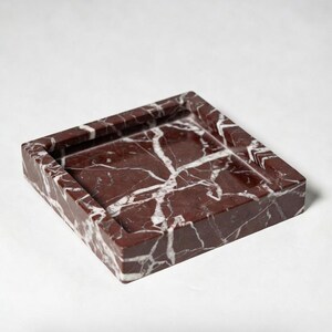 May include: A square Rosso Levanto marble tray featuring deep red tones with prominent white veining. The tray has a raised border and measures 6 inches by 6 inches by 1 inch as indicated by the text printed below the object in the image.
