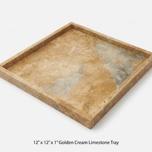 May include: A square, golden cream limestone tray, measuring 12 inches by 12 inches, with a 1-inch depth. The tray has a natural, textured surface with variations of tan, cream, and gray tones. The edges are neatly framed.