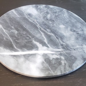 May include: A round, grey marble serving tray with white veining. The tray is smooth and polished.