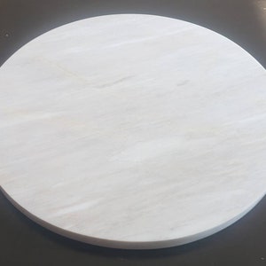 May include: A round white marble serving tray with a smooth surface and subtle veining.