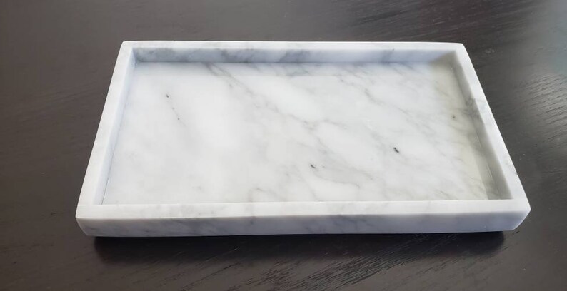 May include: A white marble rectangular tray with a raised rim. The tray has a natural veining pattern.