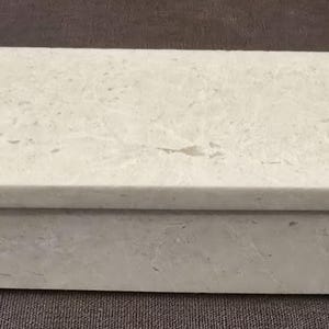 Puede incluir: Una caja rectangular blanca con tapa. La caja est&aacute; hecha de un material texturizado que se asemeja a la piedra.