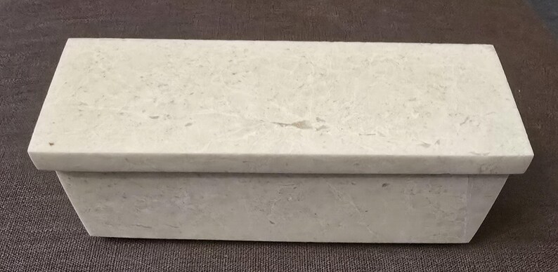 Puede incluir: Una caja rectangular blanca con tapa. La caja est&aacute; hecha de un material texturizado que se asemeja a la piedra.