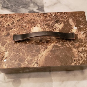 May include: A rectangular marble box with a brown and gold marbled pattern. The box has a black metal handle.