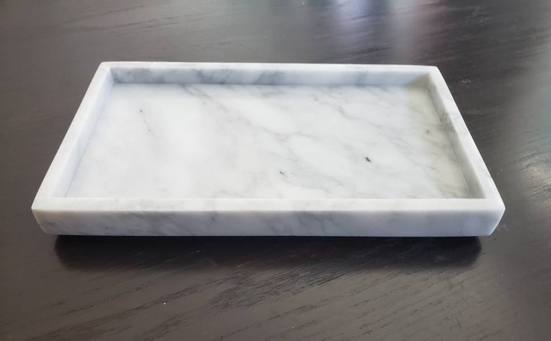 May include: A white marble tray with a rectangular shape and a smooth surface. The tray has a raised edge and is perfect for serving or displaying items.